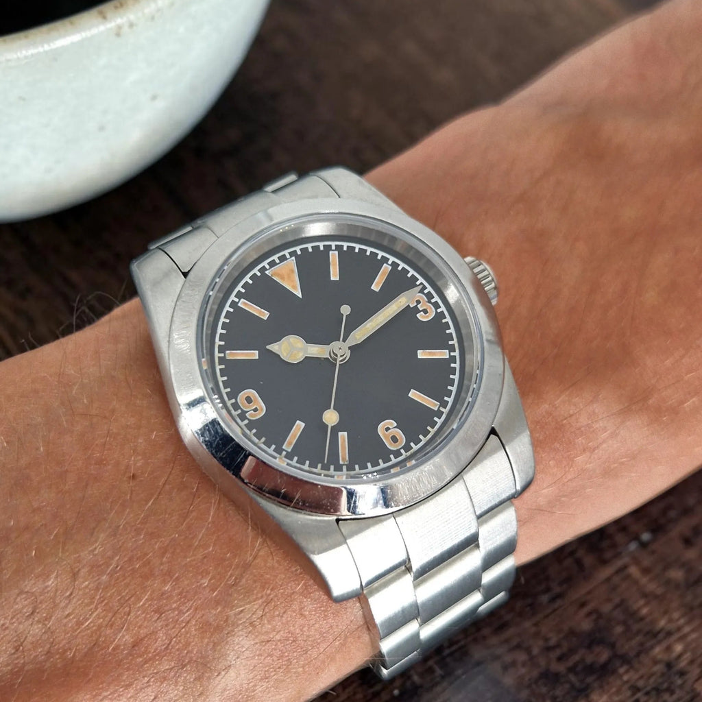 36mm vintage automatic field watch worn on the wrist beside a coffee cup