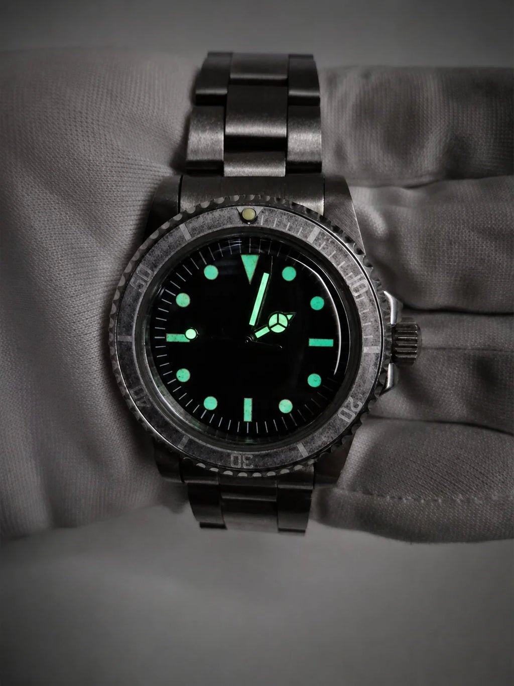 A dark stainless steel vintage watch mods ghost bezel diver wristwatch with a black dial and glowing green luminescent markers, shown resting on a gray textured surface.