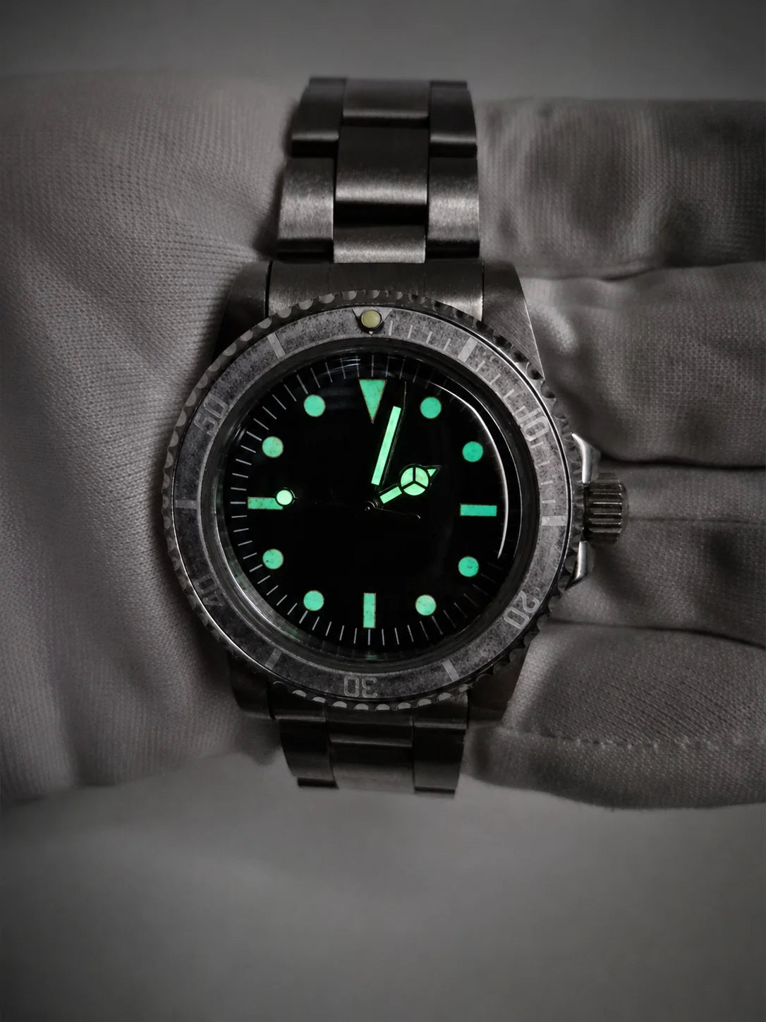 A dark stainless steel vintage watch mods ghost bezel diver wristwatch with a black dial and glowing green luminescent markers, shown resting on a gray textured surface.