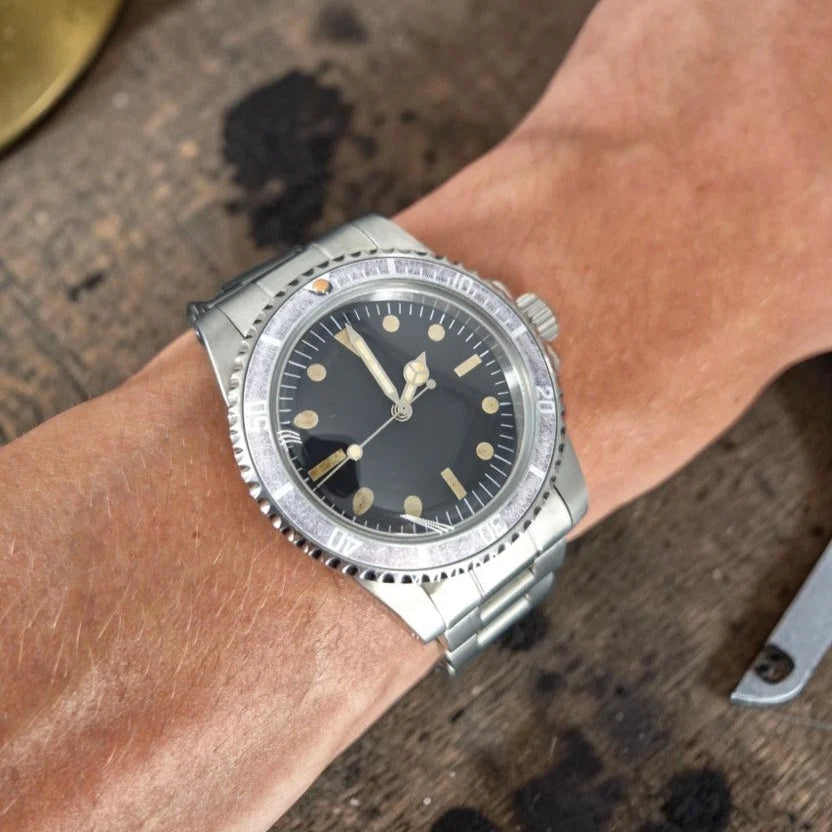 39.5mm aged ghost-bezel automatic dive watch worn on the wrist at a workbench
